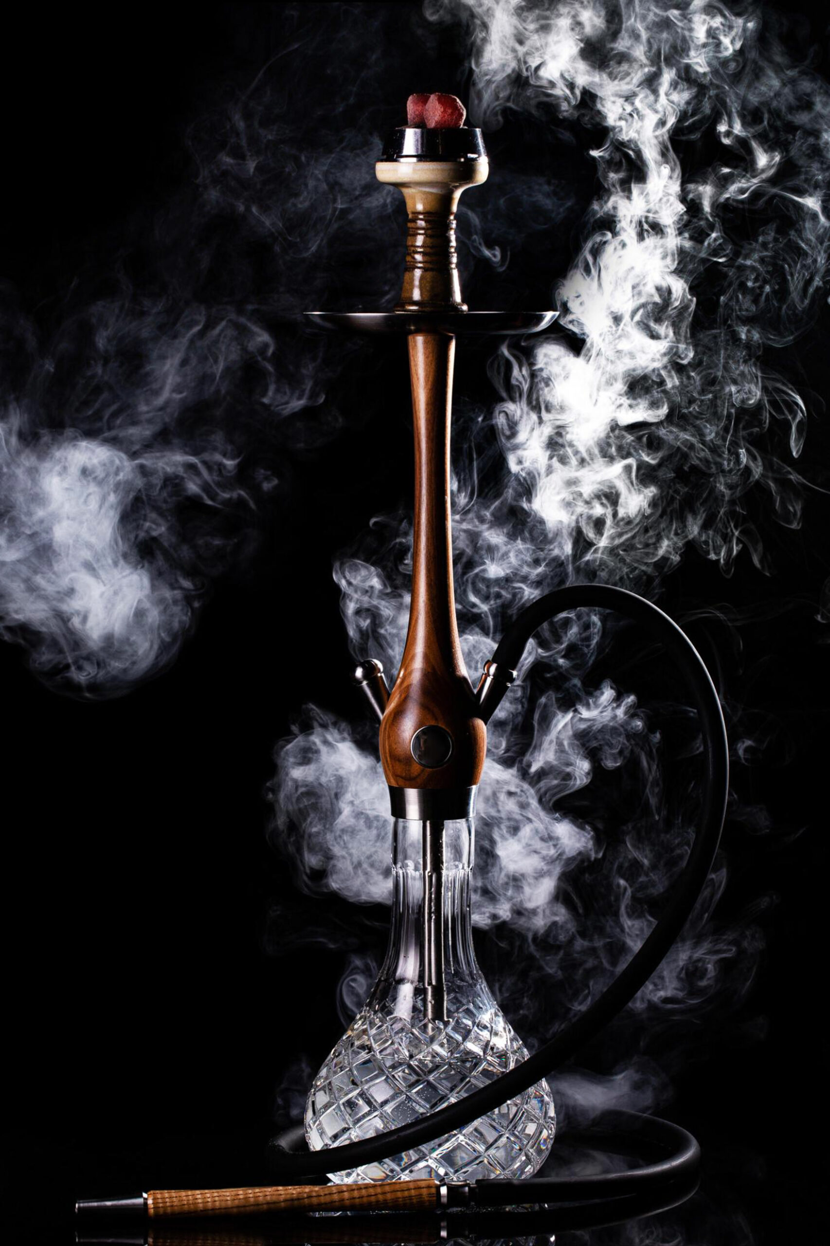 Hookah shisha with glass flask and clay bowl with white smoke on a black background. Traditional Eastern relaxation